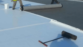 Workers installing white roof membrane on commercial rooftop.