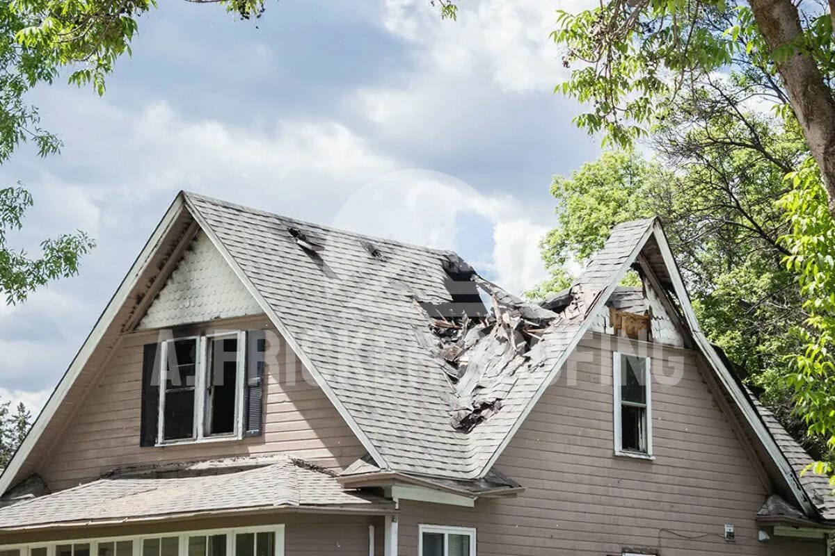 Damaged house roof with large hole from storm or tree damage, showing broken shingles