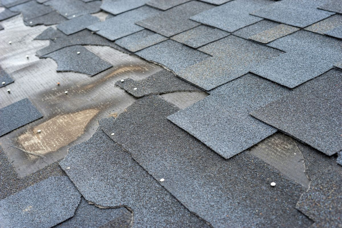 Damaged asphalt roof shingles with missing pieces and exposed underlayment