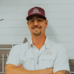 Smiling man in baseball cap and light blue shirt with crossed arms outdoors