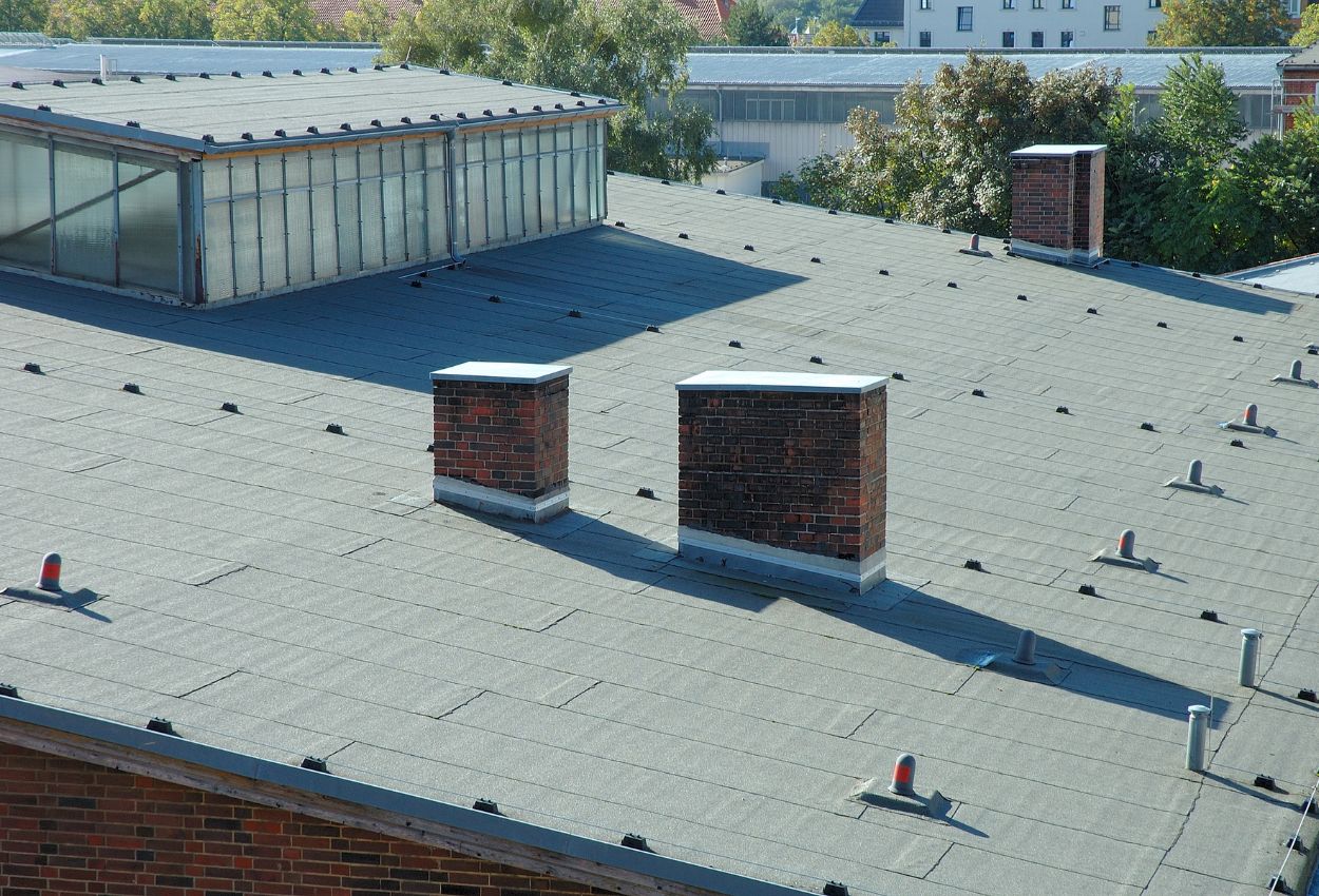 Flat gray industrial roof with brick chimneys and vent pipes.