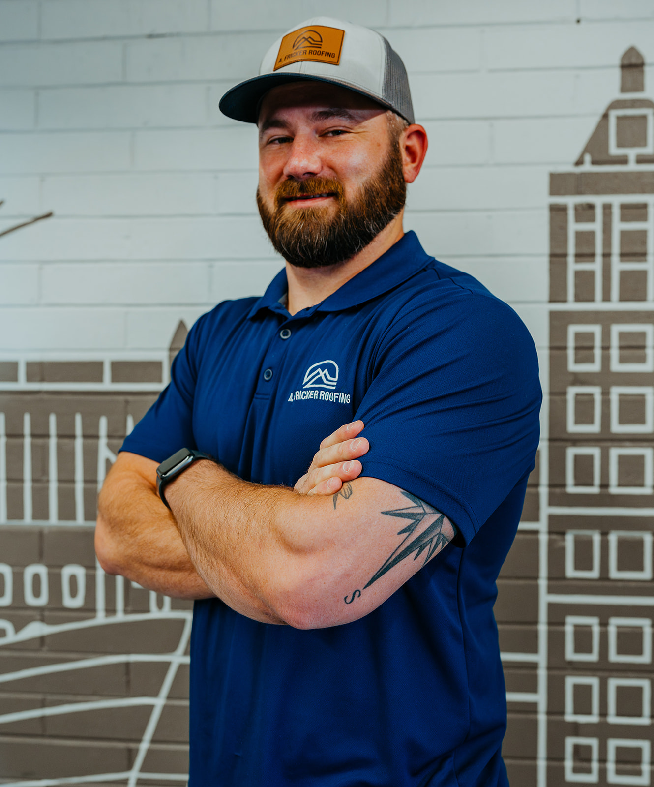 Confident man in a blue uniform shirt with arms crossed, brick wall background.