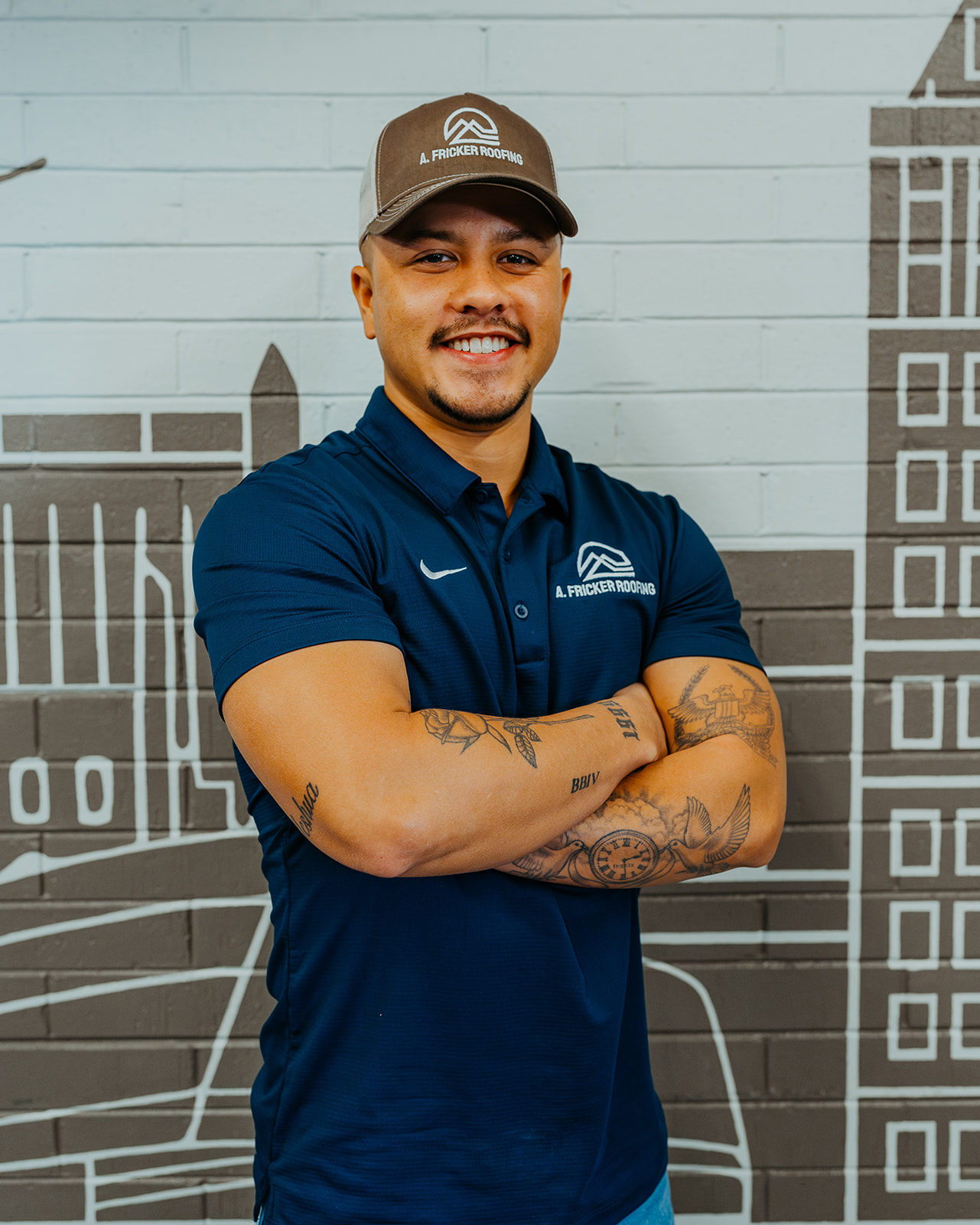 Smiling man in A. Fricker Roofing attire standing in front of a mural wall.