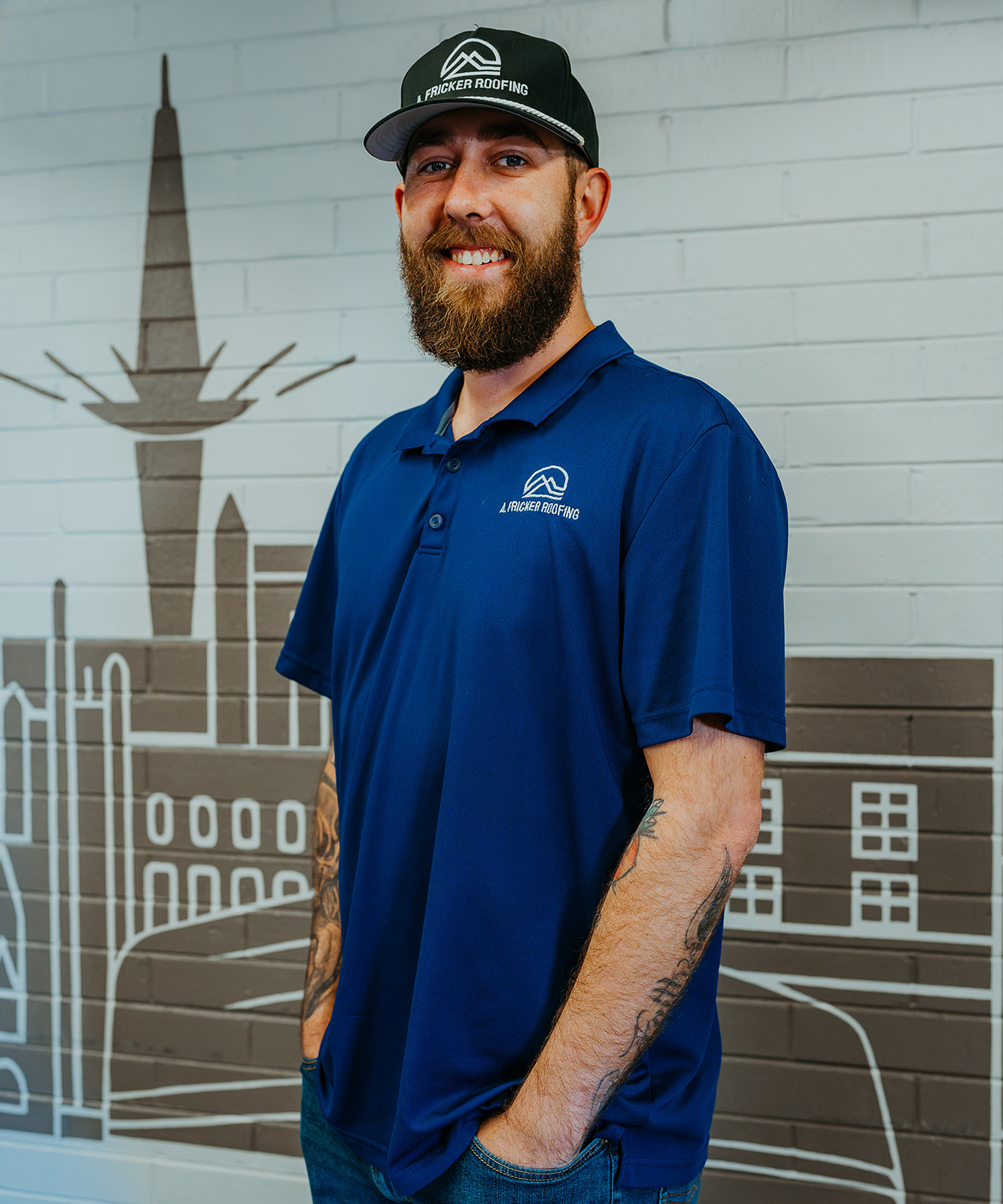 Man in blue shirt and cap standing in front of wall mural.