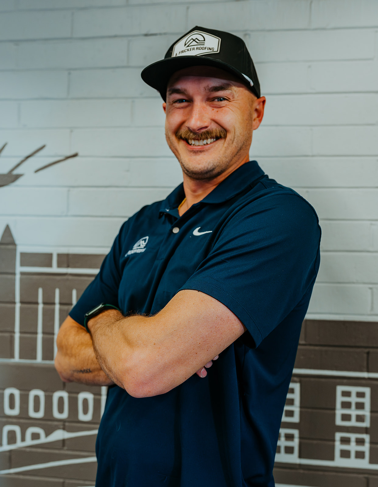 Smiling man in a navy shirt and hat standing confidently indoors.