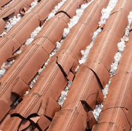 Red ceramic roof tiles with hail damage alongside packed ice.