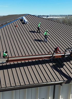 Workers installing a metal roof on a building under clear skies