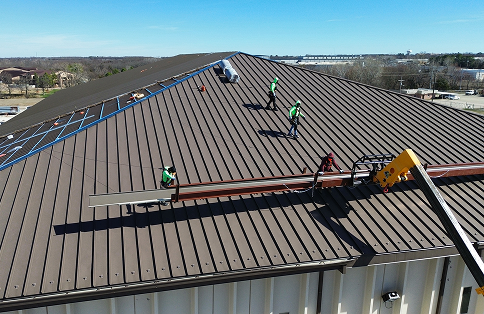 Construction workers installing panels on large metal roof of building