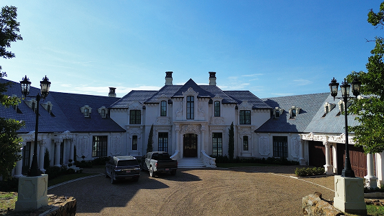 Elegant large mansion with luxury vehicles in front, under blue sky