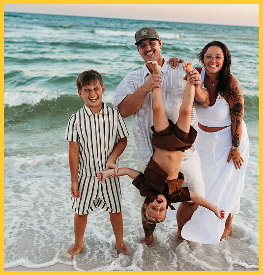 Family enjoying a playful moment at the beach with a child being held upside down.